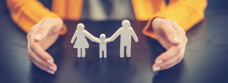 Figurine of the family surrounding by woman's hands. Concept of the care and security in relation.
