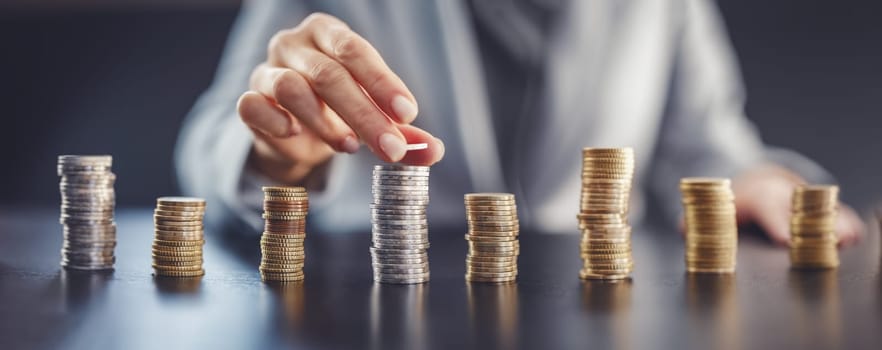 Woman sitting at the table and putting coin on the largest stack of the money. Concept of the wages and financial income in business.