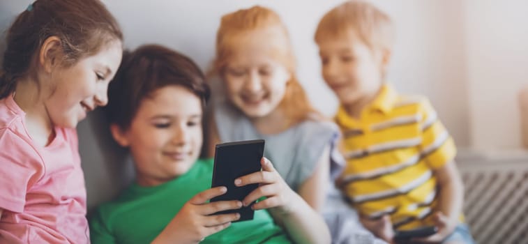 Group of children sitting indoors and looking in the smartphone. Concept of relationship, friendship and using of smart technologies.