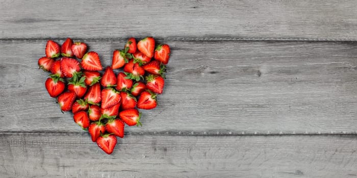 Top-down view - heart made of strawberry pieces on gray wood desk. Space for text on right.
