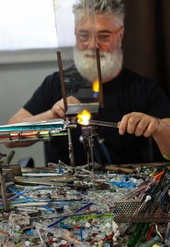 Venice, Italy - September 5, 2022: Glassworker while shaping the glass with a very high temperature flame in its artisan workshop in Venice. Italy