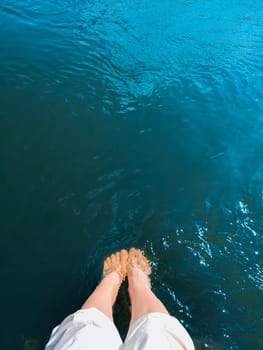 A woman lowered her feet into turquoise seawater.