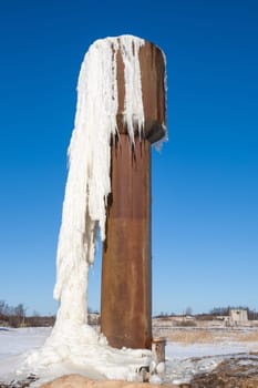 Frozen water flowing from an old water tower againt blue sky