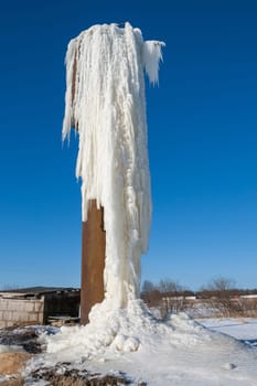 Frozen water flowing from an old water tower againt blue sky
