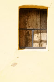 A striking window grille on a building barricaded with wood.