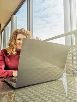 A blonde with curly hair communicates via video link on a laptop sitting in front of a window.