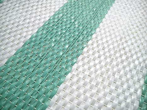 Green and white synthetic burlap, close-up. Polyethylene material. Interlacing of polyethylene fibers and threads. Striped beach mat or sports mat.