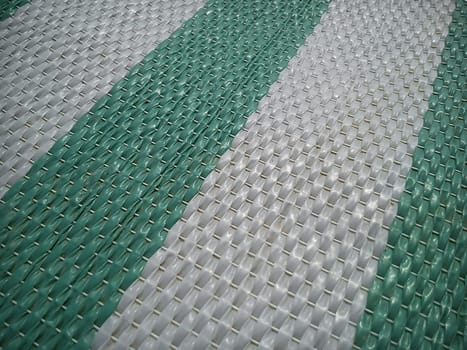 Green and white synthetic burlap, close-up. Polyethylene material. Interlacing of polyethylene fibers and threads. Striped beach mat or sports mat.