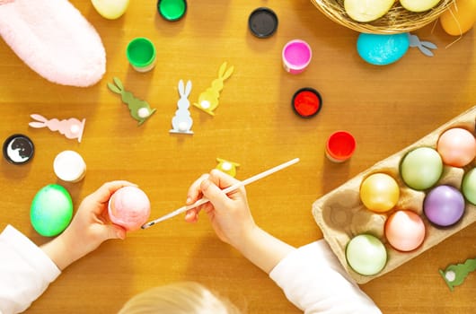 Child hands painting colored eggs for Easter on the wooden table at home. Happy Easter. Preparation for Easter. High quality photo.