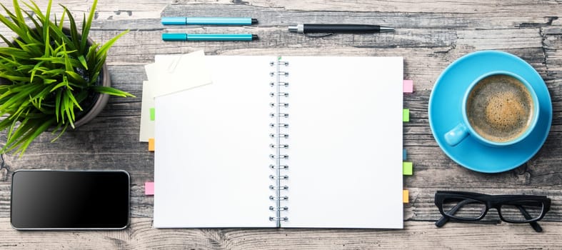 Office table with a coffee cup, a blank notepad and a plant