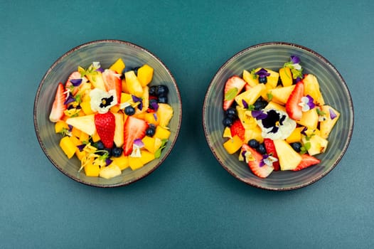 Salad of pineapple, strawberries and berries, decorated with edible flowers. Clean ealthy eating