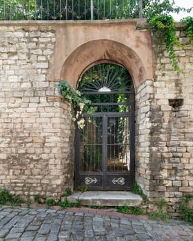 Exterior shot of grungy abandoned entrance with rusted wrought iron arched door, in a cobblestone narrow street, Balat District, Istanbul, Turkiye