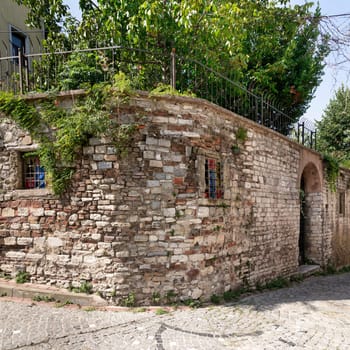 Old abandoned building, with weathered stone wall, and wrought iron windows, partially covered with climber plants, in a narrow alley with cobblestone floor, Balat district, Istanbul, Turkey
