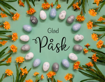 Flat Lay With Swedish Text Glad Pask Means Happy Easter. Easter Egg Decoration With Orange Spring Flowers. Light Green Paper Background.