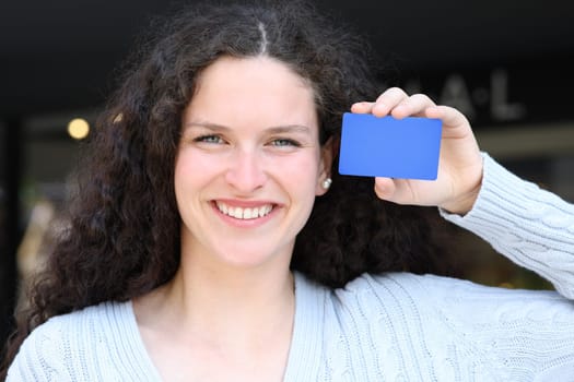 Front view portrait of a woman showing blank blue credit card in the street