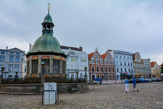 Wismar, Germany, September 10, 2022 - Street at the market square with the water art fountain in the middle of the historic Hanseatic city of Wismar, on the Baltic Sea coast of Mecklenburg-West Pomerania in Germany