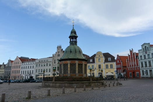 Wismar, Germany, September 10, 2022 - Street at the market square with the water art fountain in the middle of the historic Hanseatic city of Wismar, on the Baltic Sea coast of Mecklenburg-West Pomerania in Germany