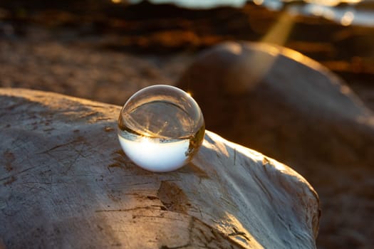 Glass ball on a rock at sunset on the beach, the sea and the setting sun are reflected in the ball