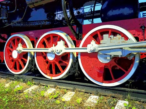 Retro vintage wheels of a locomotive or train close up. Red large heavy metal wheels with piston guiding mechanisms. Locomotive of the 19th - 20th centuries with a steam engine. Bright vivid photo.