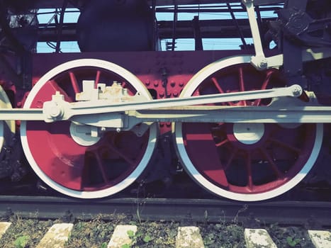 Retro vintage wheels of a locomotive or train close up. Red large heavy metal wheels with piston guiding mechanisms. Locomotive of the 19th - 20th centuries with a steam engine. Retro style