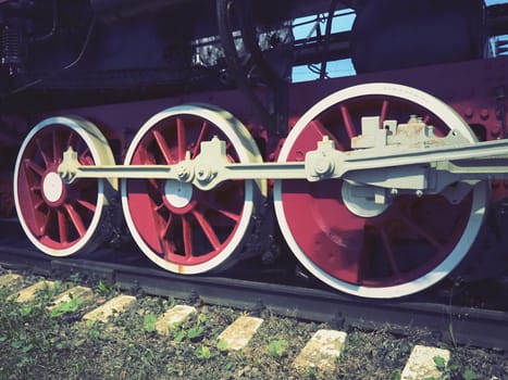 Retro vintage wheels of a locomotive or train close up. Red large heavy metal wheels with piston guiding mechanisms. Locomotive of the 19th - 20th centuries with a steam engine. Retro style.