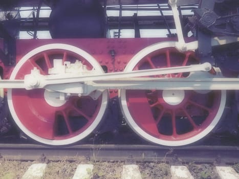 Retro vintage wheels of a locomotive or train close up. Red large heavy metal wheels with piston guiding mechanisms. Locomotive of the 19th - 20th centuries with a steam engine. Blurred soft focus.