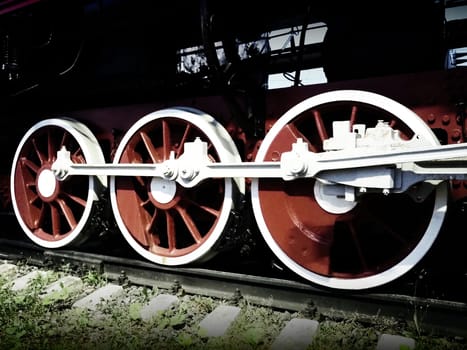 Retro vintage wheels of a locomotive or train close up. Red large heavy metal wheels with piston guiding mechanisms. Locomotive of the 19th - 20th centuries with a steam engine. Bright vivid photo.