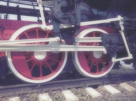 Retro vintage wheels of a locomotive or train close up. Red large heavy metal wheels with piston guiding mechanisms. Locomotive of the 19th - 20th centuries with a steam engine. Blurred soft focus.