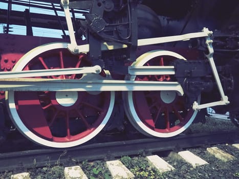 Retro vintage wheels of a locomotive or train close up. Red large heavy metal wheels with piston guiding mechanisms. Locomotive of the 19th - 20th centuries with a steam engine. Retro style
