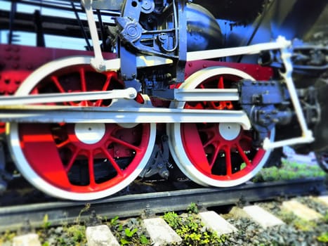 Retro vintage wheels of a locomotive or train close up. Red large heavy metal wheels with piston guiding mechanisms. Locomotive of the 19th - 20th centuries with a steam engine. Bright vivid photo.