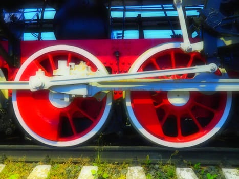 Retro vintage wheels of a locomotive or train close up. Red large heavy metal wheels with piston guiding mechanisms. Locomotive of the 19th - 20th centuries with a steam engine. Bright vivid photo.