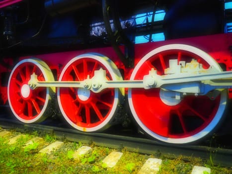 Retro vintage wheels of a locomotive or train close up. Red large heavy metal wheels with piston guiding mechanisms. Locomotive of the 19th - 20th centuries with a steam engine. Bright vivid photo.