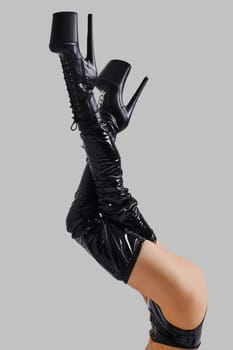 Lifted up female legs in pole dance boots on grey background