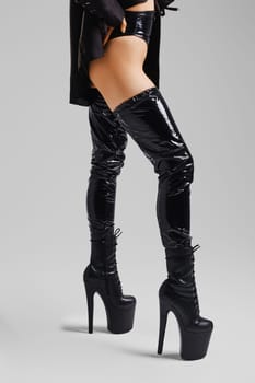 Female legs in pole dance boots standing in profile on grey background