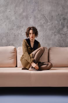 Lonely and sad young woman sits on couch with her legs crossed