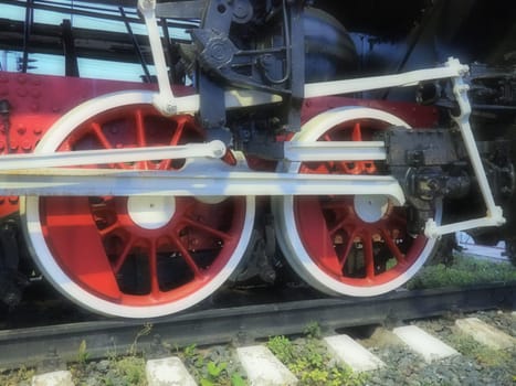 Retro vintage wheels of a locomotive or train close up. Red large heavy metal wheels with piston guiding mechanisms. Locomotive of the 19th - 20th centuries with a steam engine. Blurred soft focus.