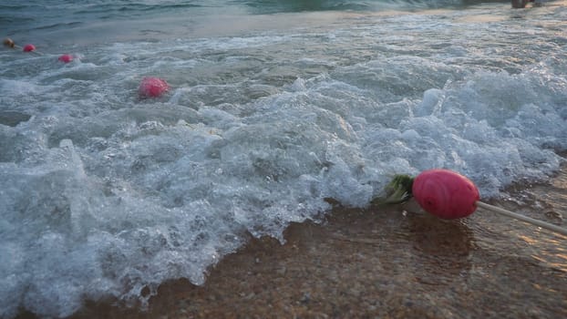 Buoys on a rope near sea water. The buoys are pink restraints to alert people to the depth of the water. Rescue of the drowning. Delimiting a place on a sandy beach between hotels. Wave with bubbles