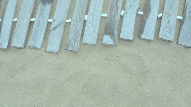 Wooden footbridge on a sandy beach. Uneven, damp wooden planks held together. The edge of the beach season at the hotel. No people, copy space. Equipped sandy beach after a storm or cyclone. Tourism.