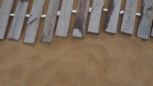 Wooden footbridge on a sandy beach. Uneven, damp wooden planks held together. The edge of the beach season at the hotel. No people, copy space. Equipped sandy beach after a storm or cyclone. Tourism.