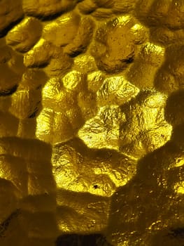 golden yellow corrugated glass with a light and dark background. reflections of light. Corrugated glass, rear light source. Play of glare and reflections on a transparent uneven surface