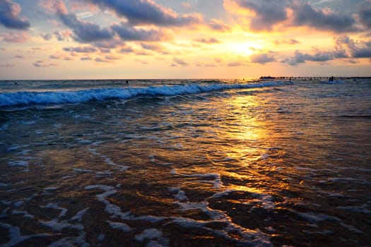 Wave and sunset over sea. Beautiful sunset. Foamy waves roll over the sandy shore. Vityazevo, Anapa, Black Sea. Tourist mecca, health resort. Evening sky. The rays reflect off the water.