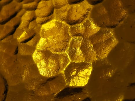 golden yellow corrugated glass with a light and dark background. reflections of light. Corrugated glass, rear light source. Play of glare and reflections on a transparent uneven surface