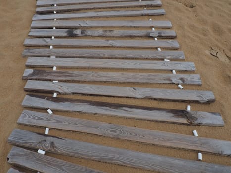 Wooden footbridge on a sandy beach. Uneven, damp wooden planks held together. The edge of the beach season at the hotel. No people, copy space. Equipped sandy beach after a storm or cyclone. Tourism.