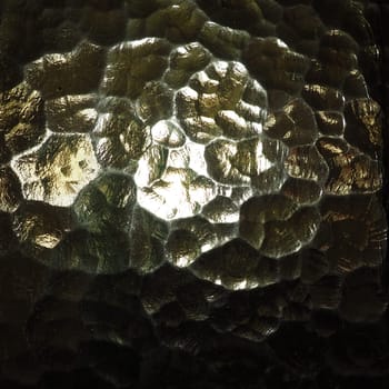 Corrugated glass, rear light source. Play of glare and reflections on a transparent uneven surface. Dark and light abstract asymmetric multi-illuminated planes. Abstract bumpy golden background