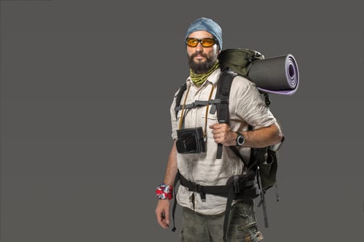 Portrait of a male fully equipped tourist with backpack and the camera on gray background