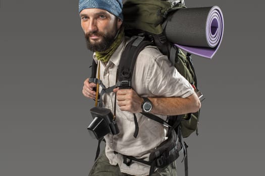 Portrait of a male fully equipped tourist with backpack and the camera on gray background