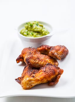 Grilled chicken wings with guacamole on white plate