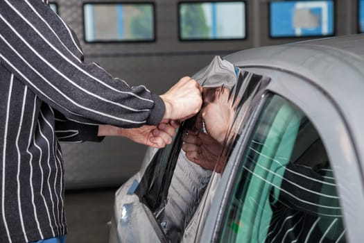 Applying tinting foil on a car window in a garage