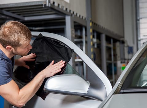 Applying tinting foil onto a car window in a workshop