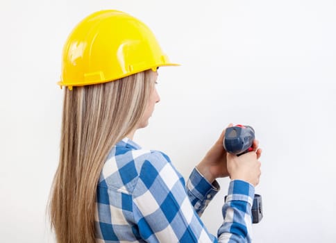 Young woman drilling a hole in the wall and wearing a protective helmet